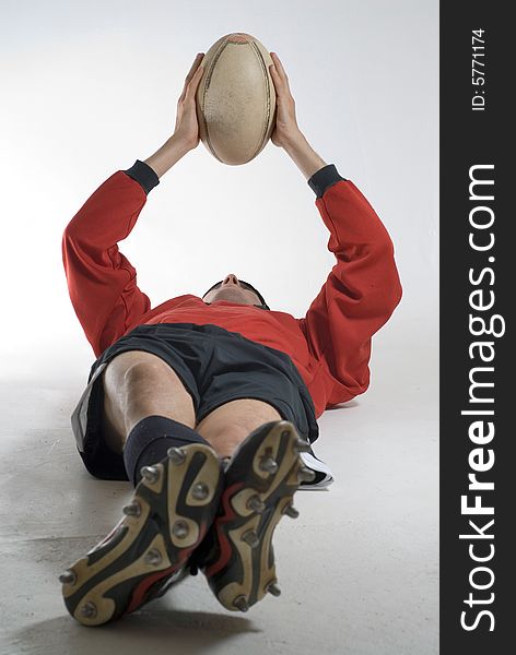 Man relaxing on the floor holding a football above his head. Vertically framed photograph. Man relaxing on the floor holding a football above his head. Vertically framed photograph