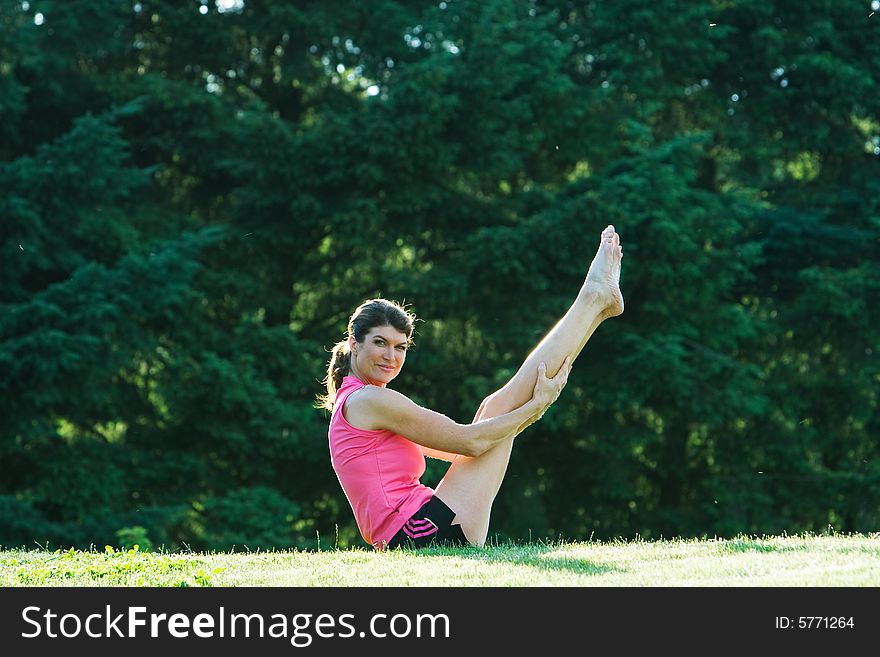 A woman sitting on a grassy lawn, with her feet and her arms in the air - Horizontally framed photograph. A woman sitting on a grassy lawn, with her feet and her arms in the air - Horizontally framed photograph.