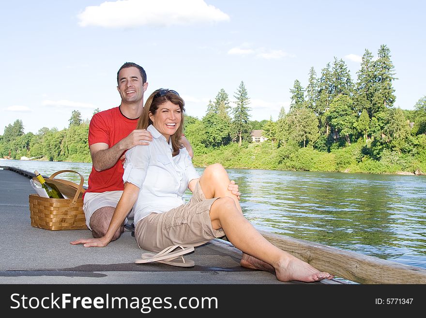 Happy couple sitting together by a lake with a picnic basket. Horizontally framed photograph. Happy couple sitting together by a lake with a picnic basket. Horizontally framed photograph