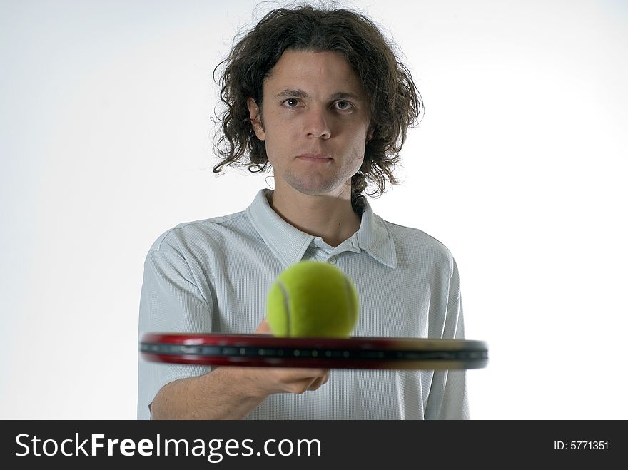 Man wearing a serious expression on his face holds a tennis racket and balances a tennis ball on top of it. Horizontally framed photograph. Man wearing a serious expression on his face holds a tennis racket and balances a tennis ball on top of it. Horizontally framed photograph