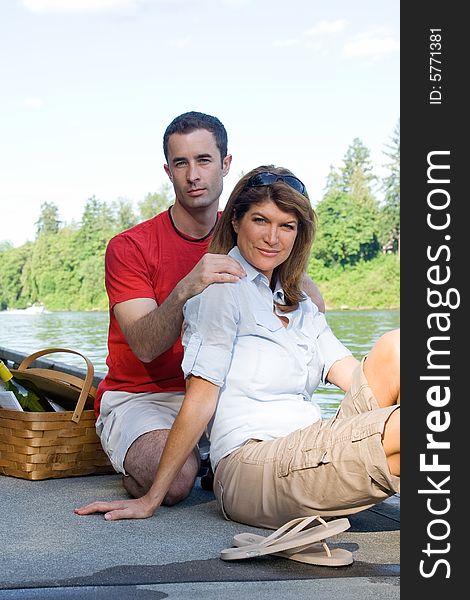 Happy couple smiling as they relax by the lake with a picnic basket next to them. Vertically framed photograph. Happy couple smiling as they relax by the lake with a picnic basket next to them. Vertically framed photograph