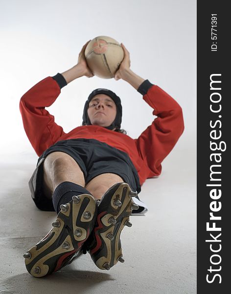 A rugby player lying on the ground holding the ball over his head. His ankles are crossed and he is looking at the camera. Vertically framed shot. A rugby player lying on the ground holding the ball over his head. His ankles are crossed and he is looking at the camera. Vertically framed shot.