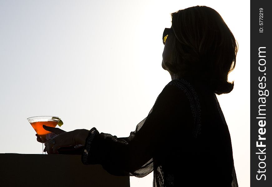 Silhouette of a woman enjoying a martini at sunset. Silhouette of a woman enjoying a martini at sunset.