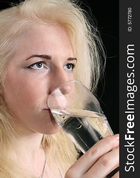 Young blond woman holds glass against the black background. Young blond woman holds glass against the black background.