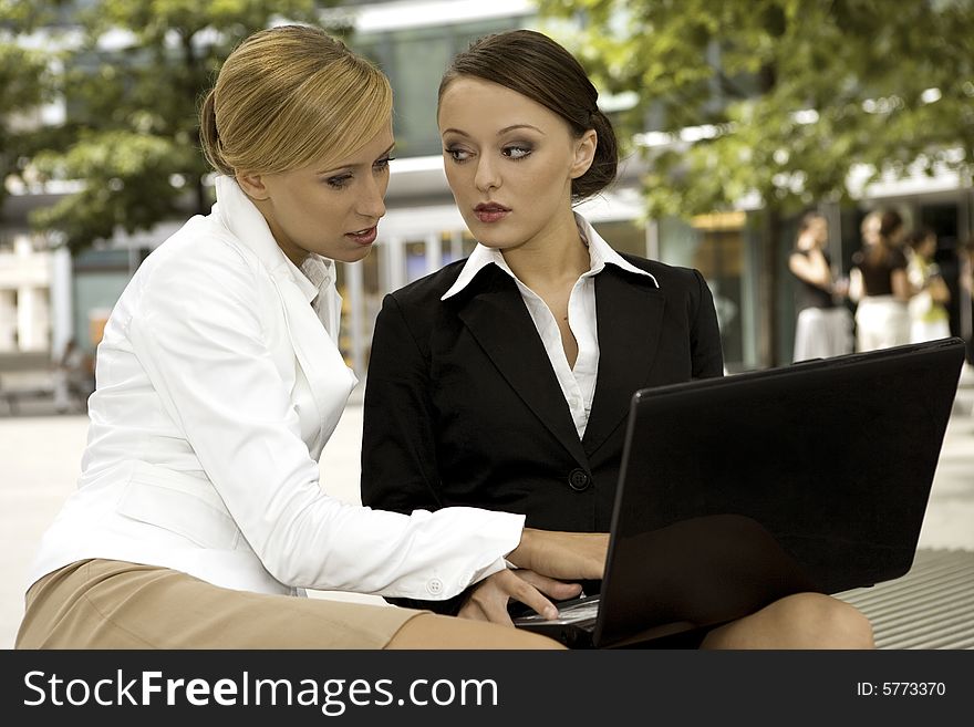 Two attractive businesswomen working on laptop outdoors. Two attractive businesswomen working on laptop outdoors