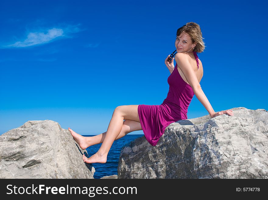 Young lady sitting on the rock in the blue sky. Young lady sitting on the rock in the blue sky