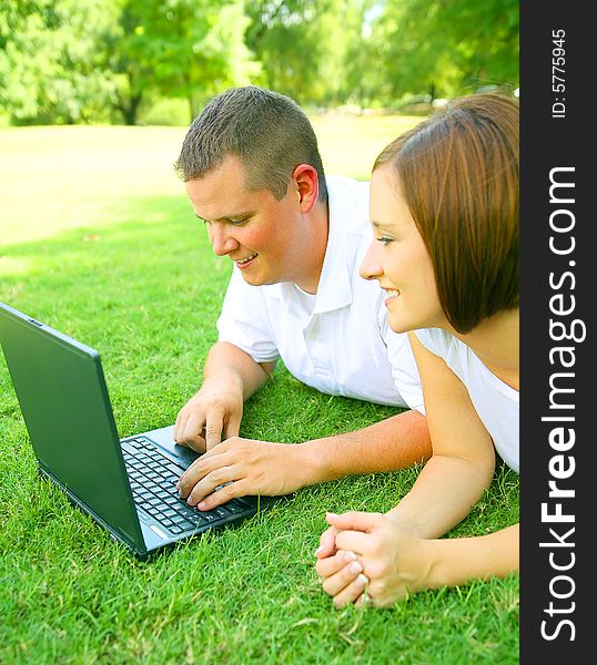 Caucasian couple using or working with computer outdoor on the grass. Caucasian couple using or working with computer outdoor on the grass