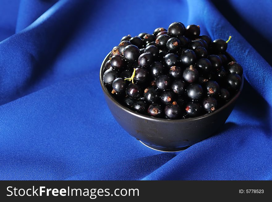 Black currants in the black bowl on the blue background. Narrow depth of field. Black currants in the black bowl on the blue background. Narrow depth of field.