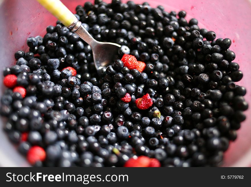 Dishful of bilberries and forest strawberries with spoon. Dishful of bilberries and forest strawberries with spoon