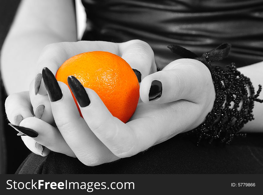 Colored mandarine in black-white hands of a gothic girl. Colored mandarine in black-white hands of a gothic girl