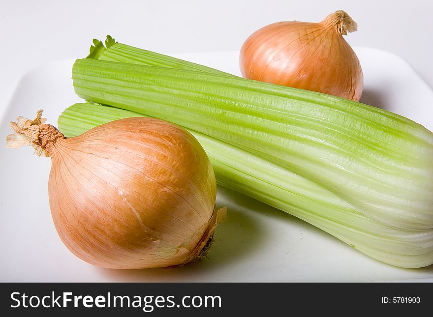 Celery and onions on a white cutting board ready to cut. Celery and onions on a white cutting board ready to cut