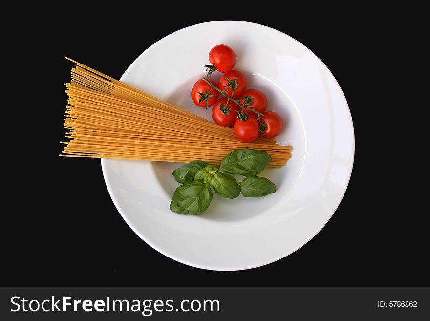 Uncooked spaghetti with small tomatoes and basil isolated on black