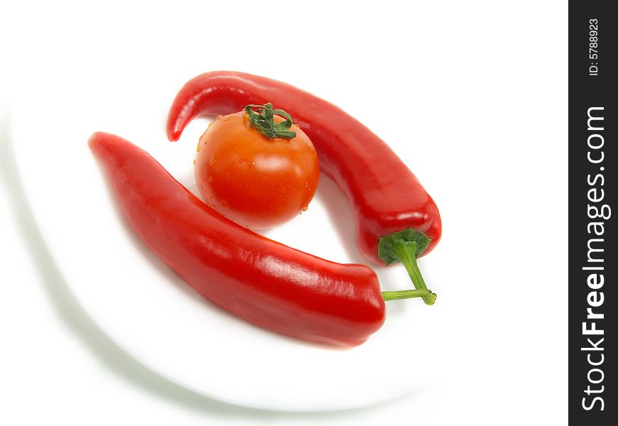 Two fresh chili peppers and a ripe tomato on a white plate and isolated on white background. Two fresh chili peppers and a ripe tomato on a white plate and isolated on white background