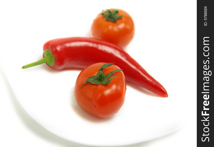 Two fresh tomatoes and a ripe chili pepper on a white plate and isolated on white background. Two fresh tomatoes and a ripe chili pepper on a white plate and isolated on white background