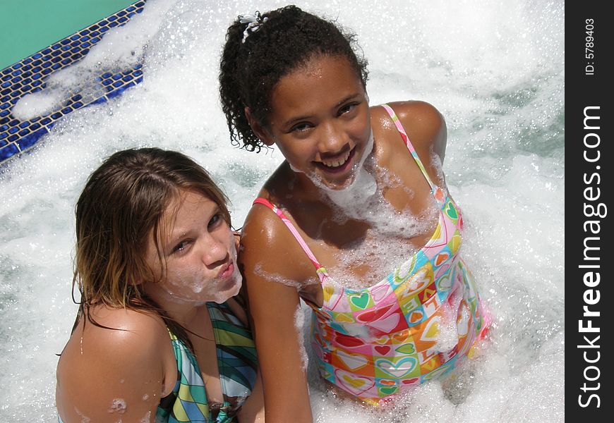 A picture of two tween girls in a jacuzzi with bubbles on them and around them. A picture of two tween girls in a jacuzzi with bubbles on them and around them.