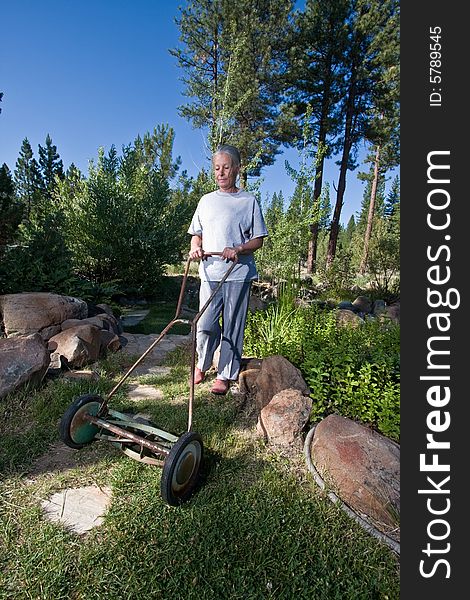 Attractive senior woman mowing lawn with hand mower