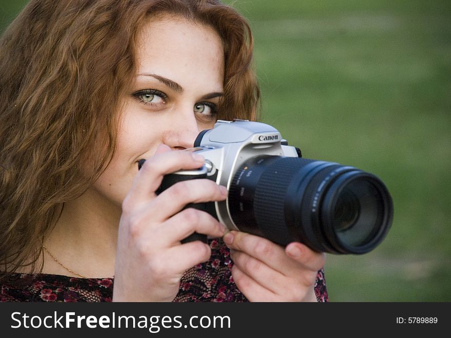 Young attractive girl, gets on the hip a camera and, enigmatically smiling, looks in a shot. Young attractive girl, gets on the hip a camera and, enigmatically smiling, looks in a shot