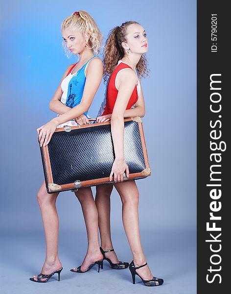 Two young beautiful girls are dressed in identical shirts hold an old suitcase. Two young beautiful girls are dressed in identical shirts hold an old suitcase