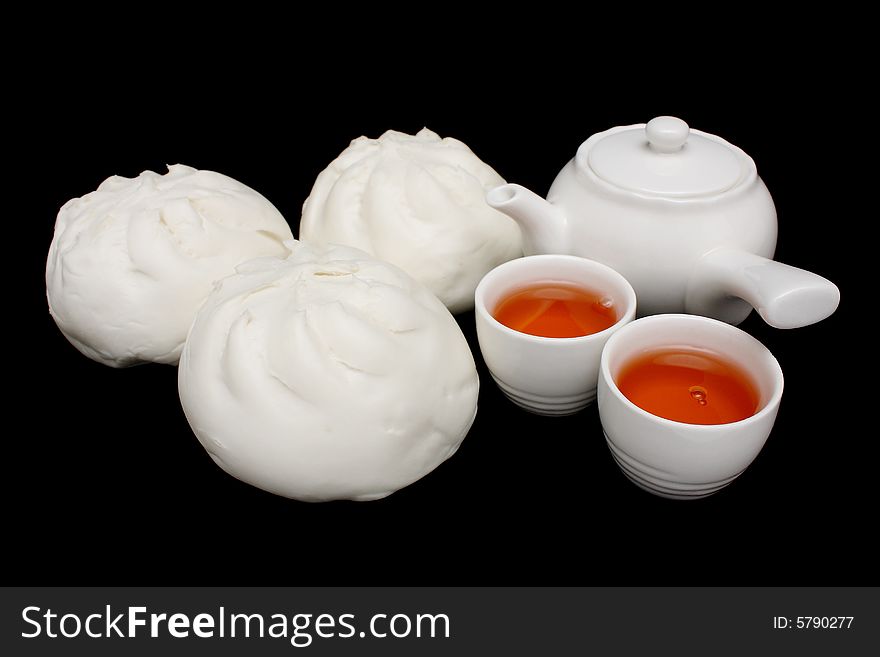 Chinese barbecued pork bun with teapot and teacups on black background.