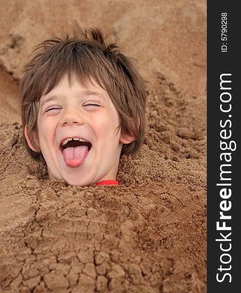 A happy young boy buried in sand at a playground. A happy young boy buried in sand at a playground