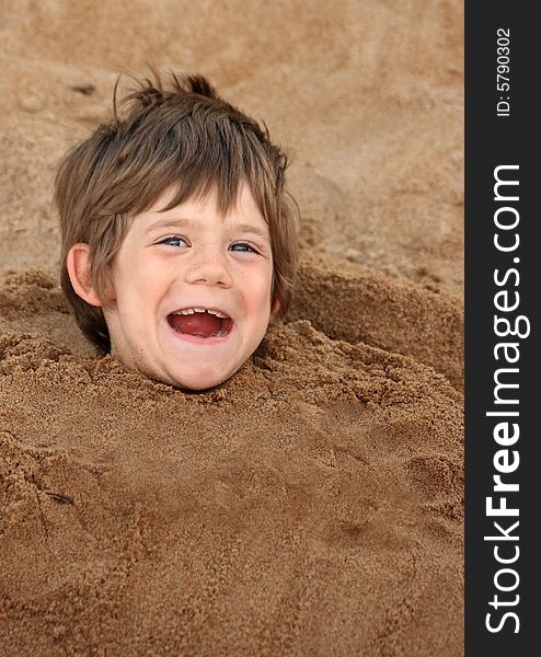 A happy young boy buried in sand at a playground. A happy young boy buried in sand at a playground