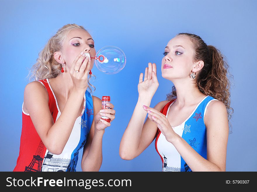 Two beautiful girls dressed in identical shirts play, inflating soap-bubbles. Two beautiful girls dressed in identical shirts play, inflating soap-bubbles