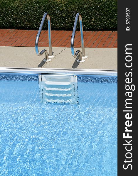 A view of white steps or ladder and metal railing going into an empty swimming pool. A view of white steps or ladder and metal railing going into an empty swimming pool.