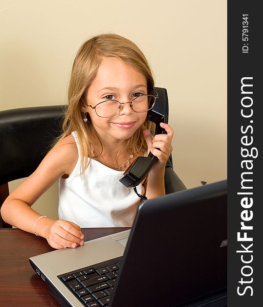 A young girl about 6 pretends to be busy at her notebook computer while wearing glasses too big for her head. A young girl about 6 pretends to be busy at her notebook computer while wearing glasses too big for her head.