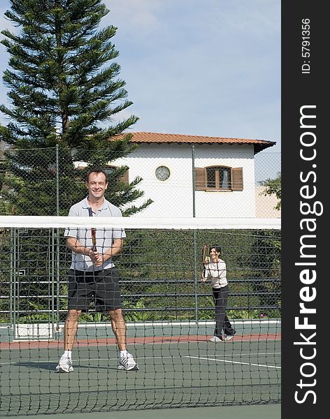 A man and woman stand on one side of the tennis court, getting ready to play tennis. - vertically framed. A man and woman stand on one side of the tennis court, getting ready to play tennis. - vertically framed