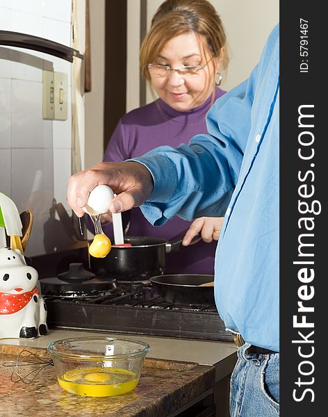 A couple cooking together.  The woman is smiling and stirring a pot on the stove.  The man is cracking an egg into a bowl. Vertically framed shot. A couple cooking together.  The woman is smiling and stirring a pot on the stove.  The man is cracking an egg into a bowl. Vertically framed shot.