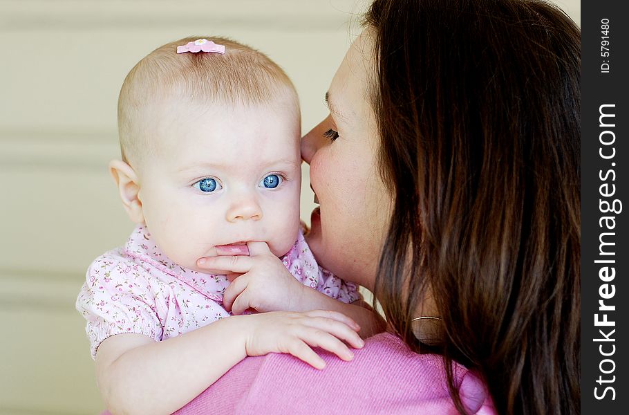 A mother, looks at her baby, and smiles. The baby looks back behind her moms shoulder, sticking her finger in her mouth. Horizontally framed shot. A mother, looks at her baby, and smiles. The baby looks back behind her moms shoulder, sticking her finger in her mouth. Horizontally framed shot.