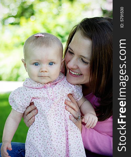 A mother and baby, both dressed in pink. The mother, playing with her child and the baby smiling at the camera. Vertically framed shot. A mother and baby, both dressed in pink. The mother, playing with her child and the baby smiling at the camera. Vertically framed shot.