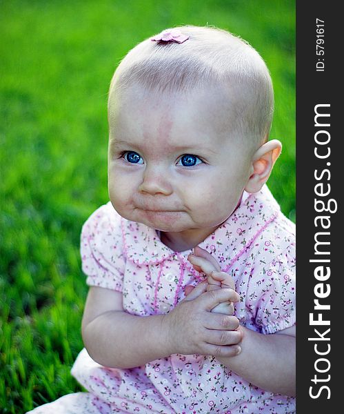 A young baby, dress in pink, holds her hands, appearing to be thinking, and smiling. Vertically framed shot. A young baby, dress in pink, holds her hands, appearing to be thinking, and smiling. Vertically framed shot.