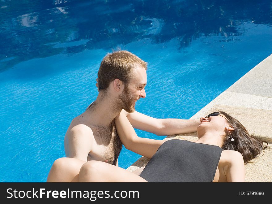 A young couple near the pool. A young woman, lies on the pools edge, while a young man stands in the pool's water, both staring and touching each other. - horizontally framed. A young couple near the pool. A young woman, lies on the pools edge, while a young man stands in the pool's water, both staring and touching each other. - horizontally framed
