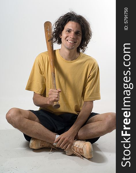 A young man, sits on the floor, folding his legs, smiling while holding a wooden bat. Vertically framed shot. A young man, sits on the floor, folding his legs, smiling while holding a wooden bat. Vertically framed shot.