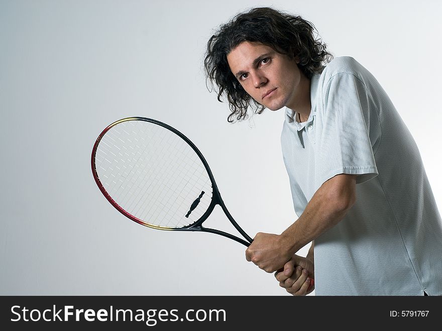 A young man, standing, holds a tennis racket as if he is about to hit a ball. Horizontally framed shot. A young man, standing, holds a tennis racket as if he is about to hit a ball. Horizontally framed shot.