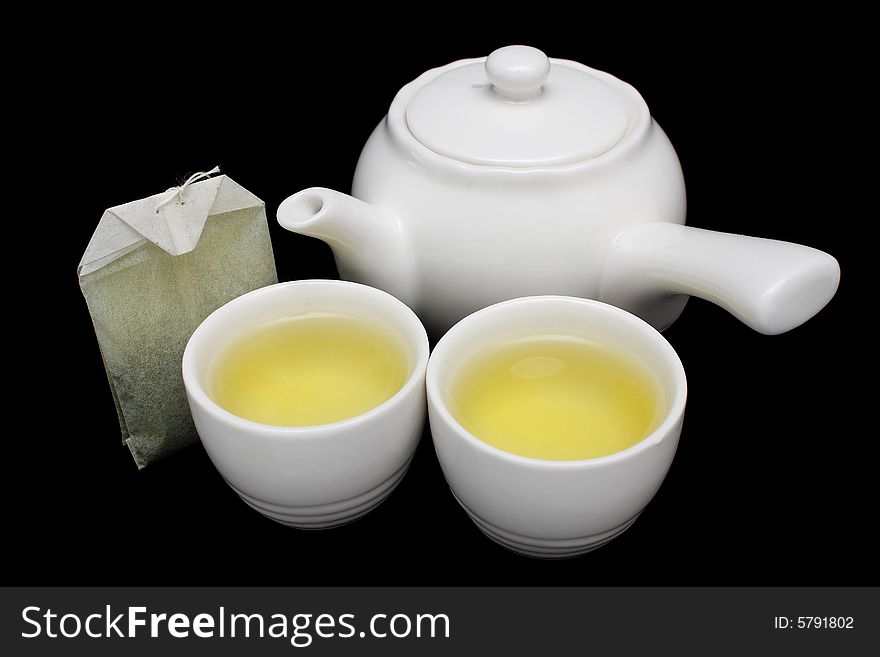 Green tea in a teacup with white teapot on black background. Green tea in a teacup with white teapot on black background.