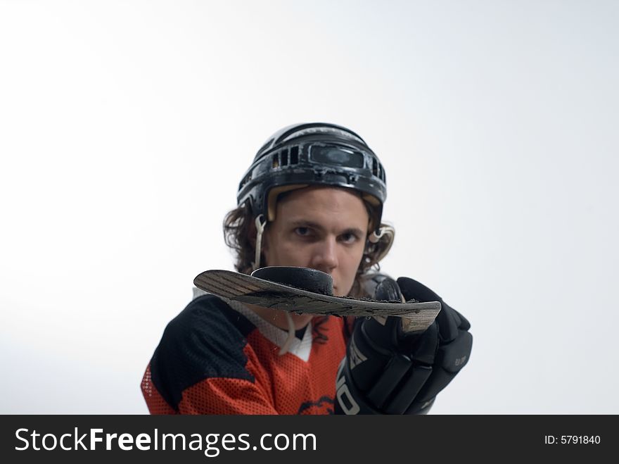 A man stands looking serious, wearing a hockey uniform. He holds out his hockey stick, balancing a puck. Horizontally framed shot. A man stands looking serious, wearing a hockey uniform. He holds out his hockey stick, balancing a puck. Horizontally framed shot.