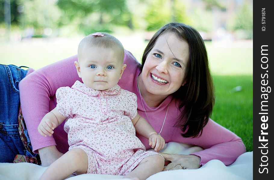 A mother and her baby, sit and lie down in a patch of grass, smiling. Horizontally framed shot. A mother and her baby, sit and lie down in a patch of grass, smiling. Horizontally framed shot.