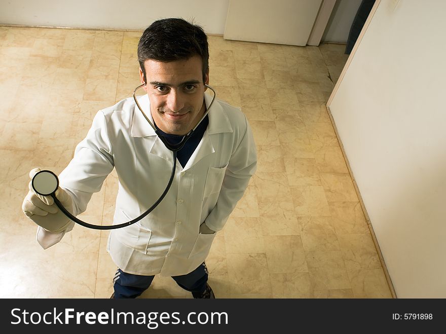 A young male doctor, stands, looking at the camera, holding his stethoscope. - horizontally framed. A young male doctor, stands, looking at the camera, holding his stethoscope. - horizontally framed