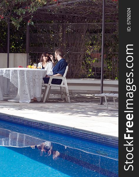 Couple Sitting At Table By Pool - Vertical