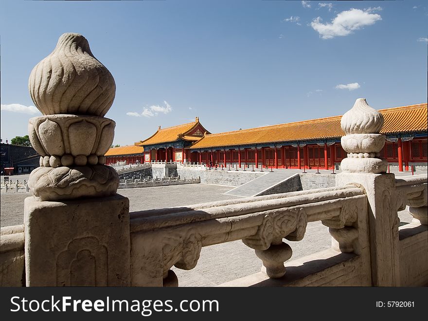 Wide angle view of emperor's palace in the forbidden city, Beijing, China, with white decorated railings in the foreground. Sunny blue sky and red / orange buildings.