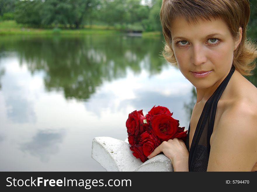 Attractive young woman with red flowers against lake reflection