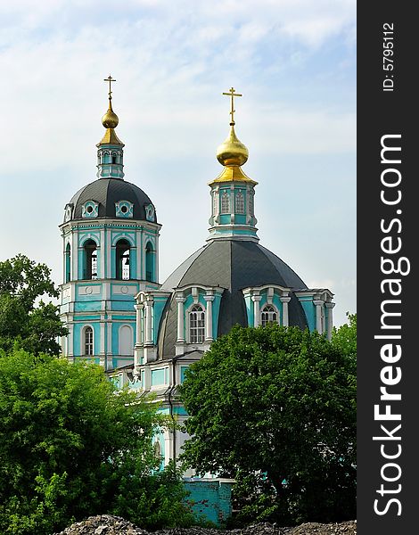 A photo of an Orthodox Church with green walls and golden domes stand behind the trees. A photo of an Orthodox Church with green walls and golden domes stand behind the trees