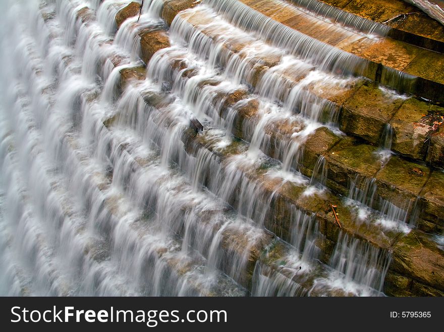 View of reservoir spillway with water tumbling over cement steps.