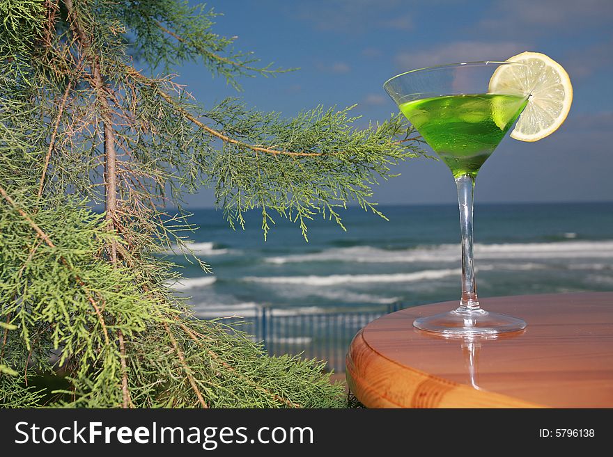 Tropical drink with the lobule of lemon in beautiful glass stands on a wooden table ashore exterminating. Tropical drink with the lobule of lemon in beautiful glass stands on a wooden table ashore exterminating