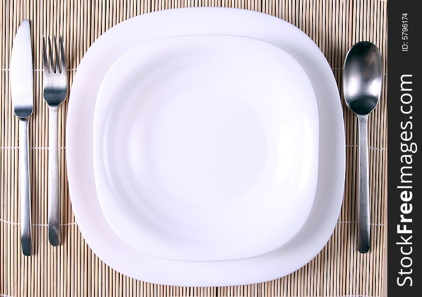 A white plate with cutlery on bamboo