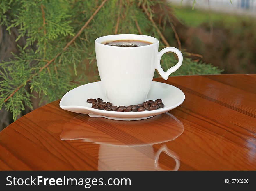 Fragrant black coffee in a stylish white cup on a glossy wooden table