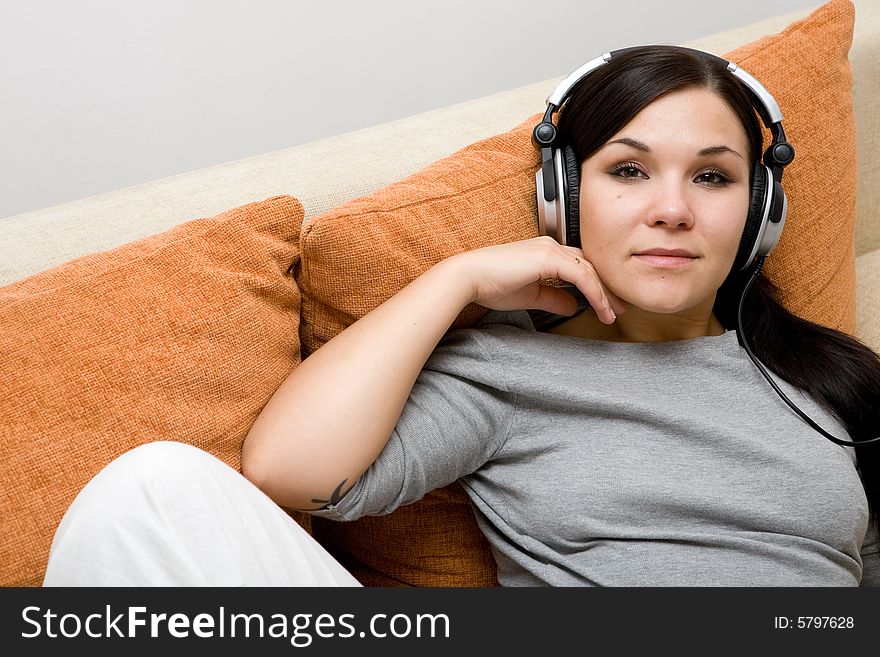 Attractive brunette woman with headphones on sofa. Attractive brunette woman with headphones on sofa