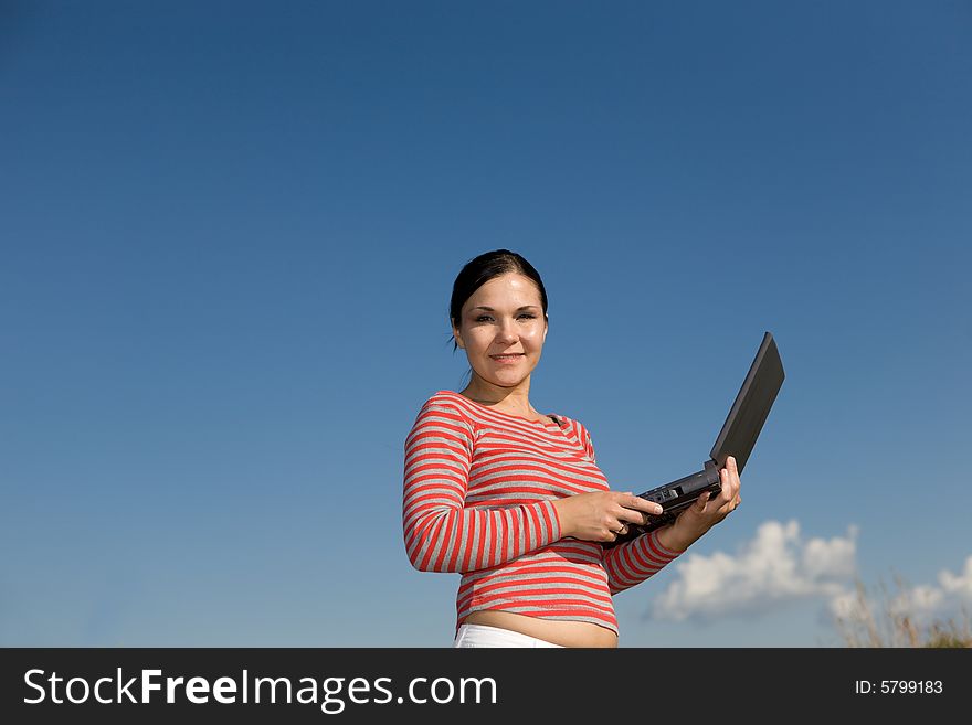 Attractive brunette woman with laptop on sky background